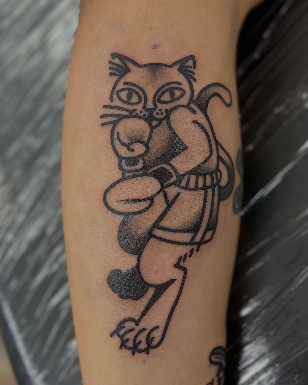 A cartoon cat in bold traditional linework on a forearm, by Kevin Lewis