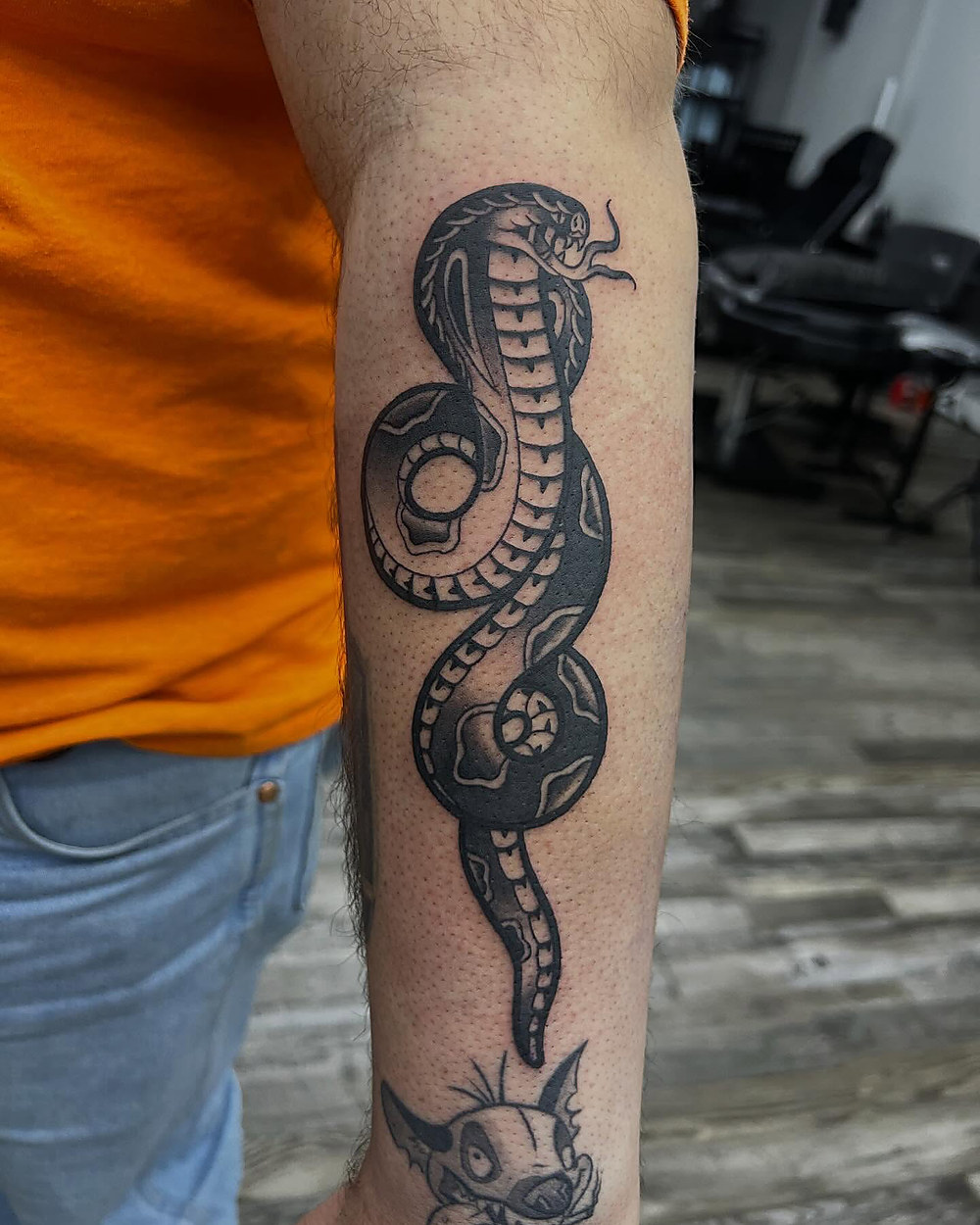 A traditional cobra winding down a forearm, by Kevin Lewis