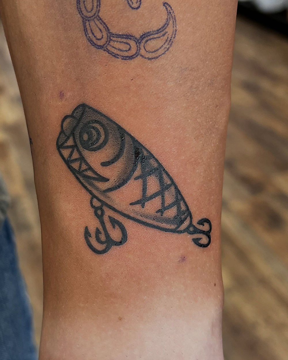 A fishing lure in bold linework on a forearm, by Kevin Lewis