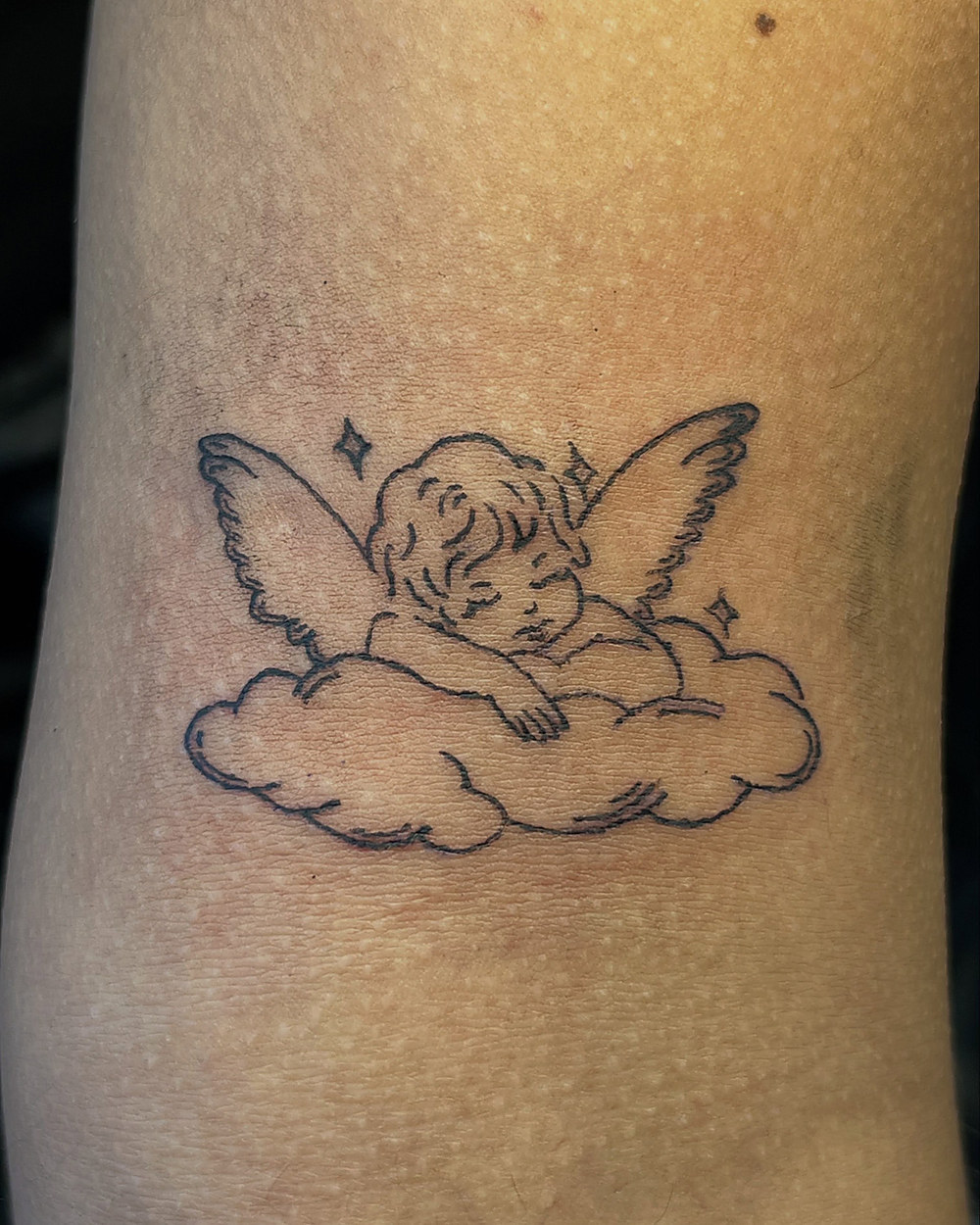 A cherub resting on a cloud, fine line on an arm, by Miah