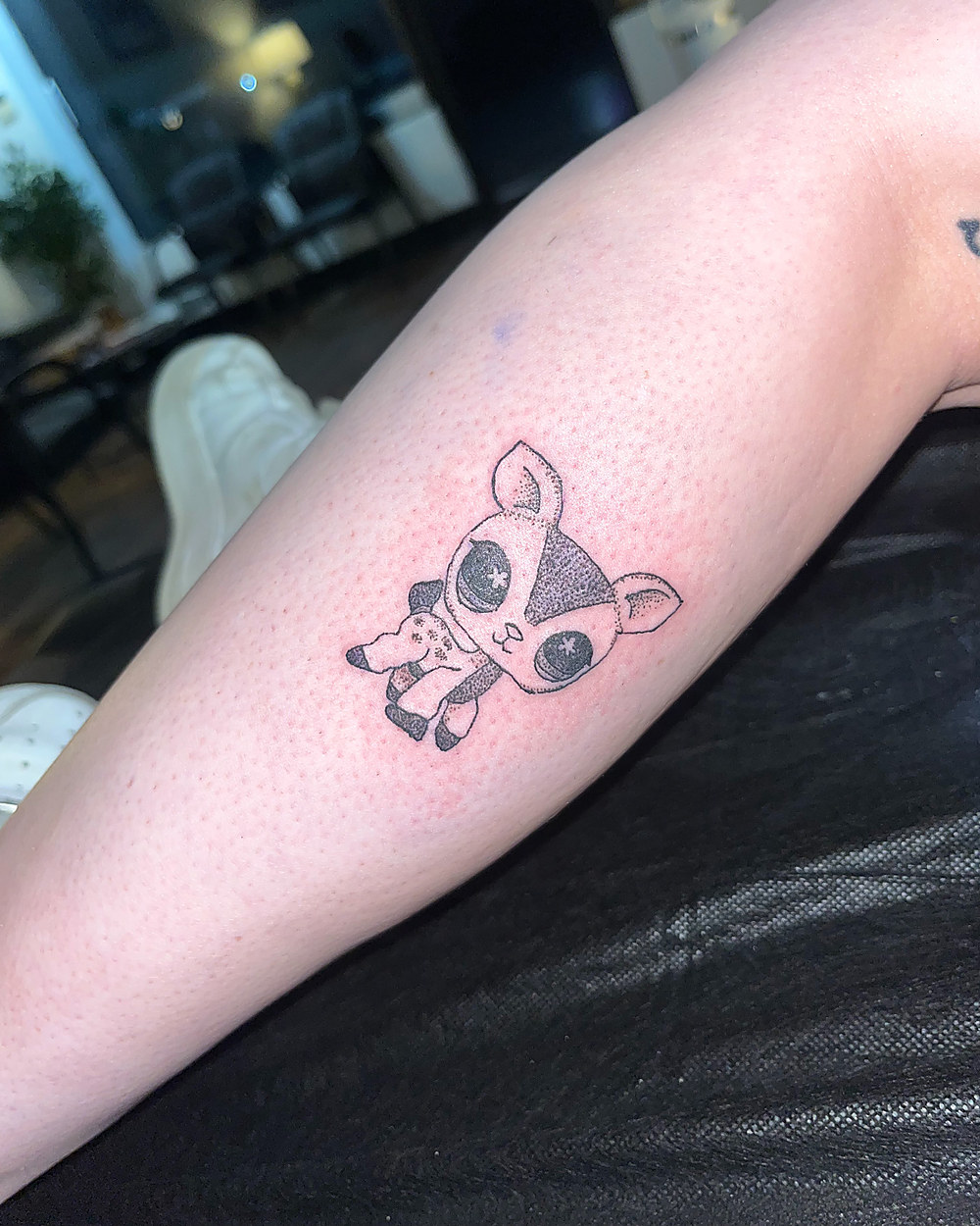 A small cartoon cow in fine line on a forearm, by Miah