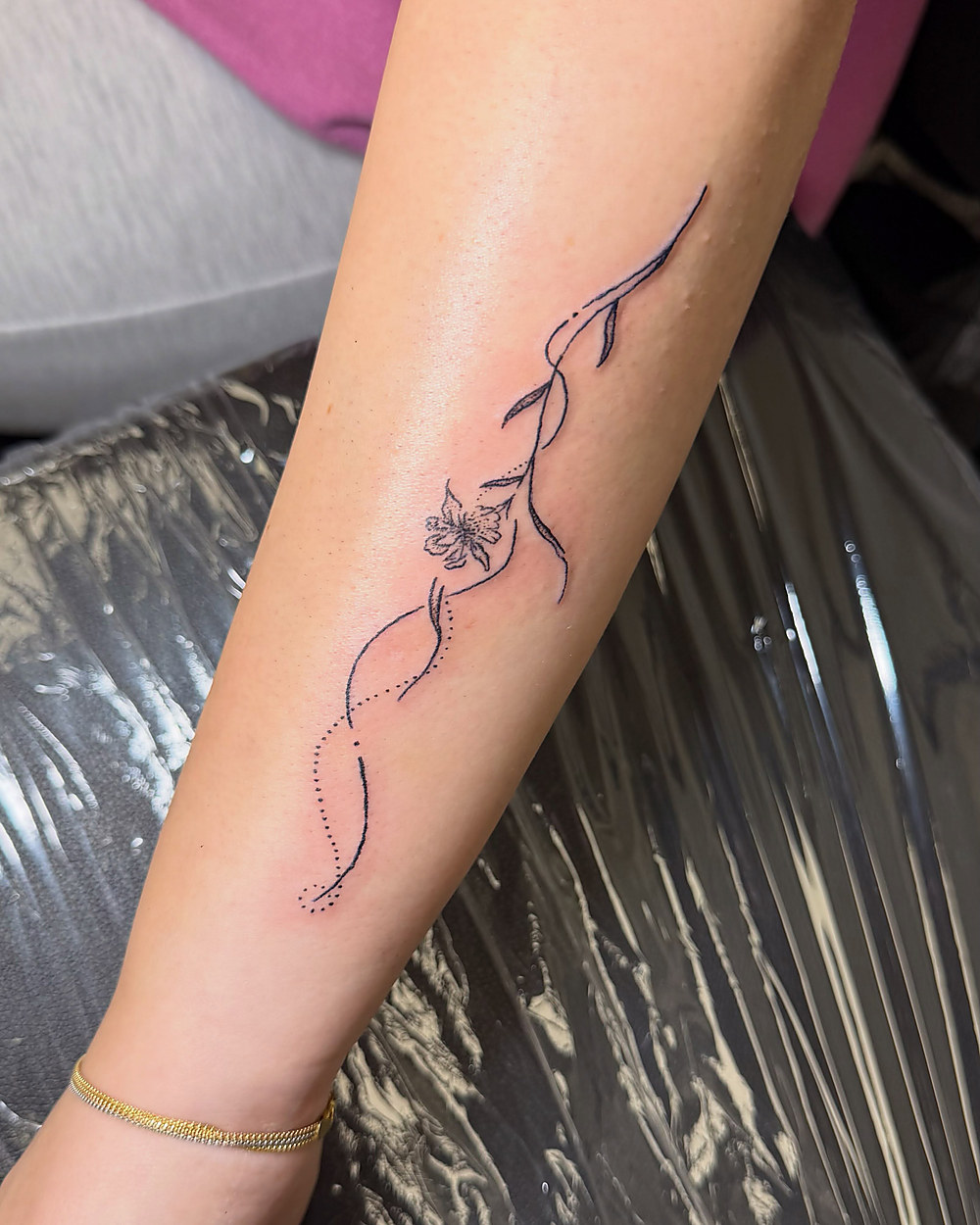 A fine line floral vine running down a forearm, by Miah