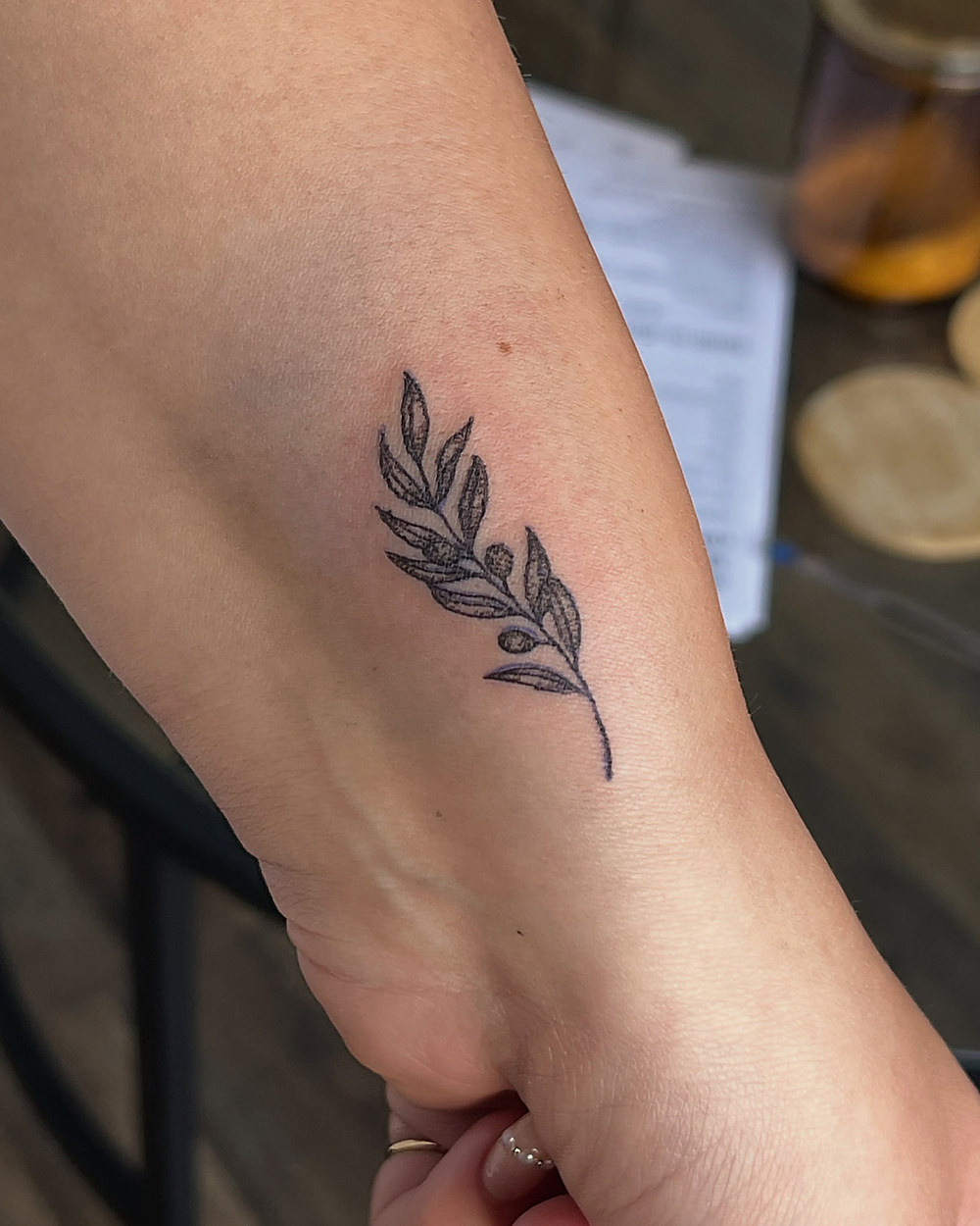 An olive branch in fine line on a forearm, by Miah
