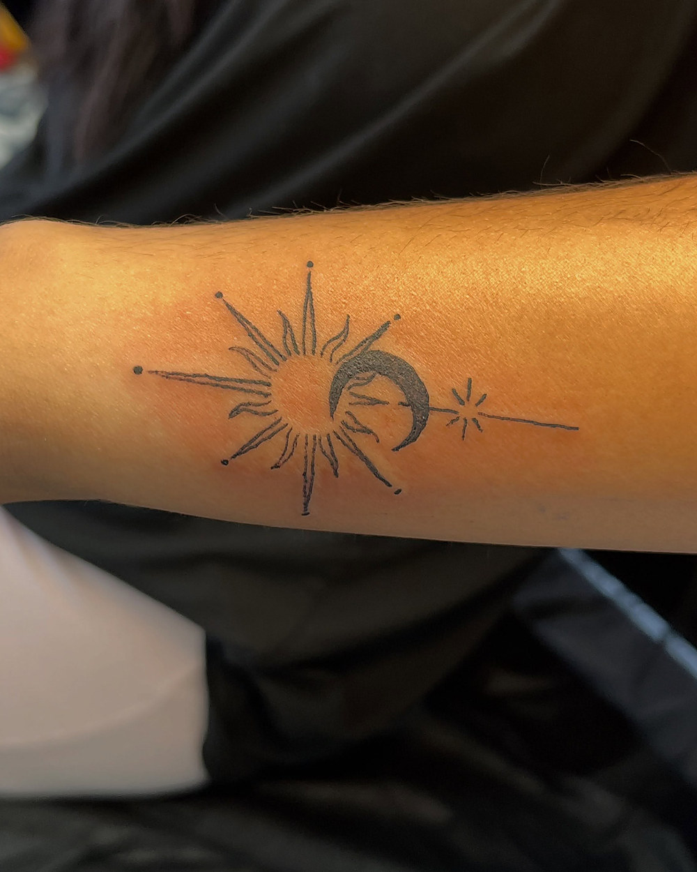 A sun, moon and sparkles in fine line on a forearm, by Miah