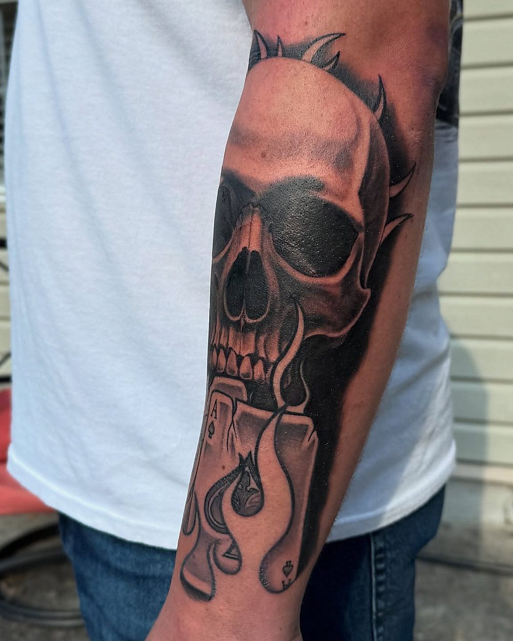 Skull and cards forearm piece, the lower half healed, by Owen Lewis