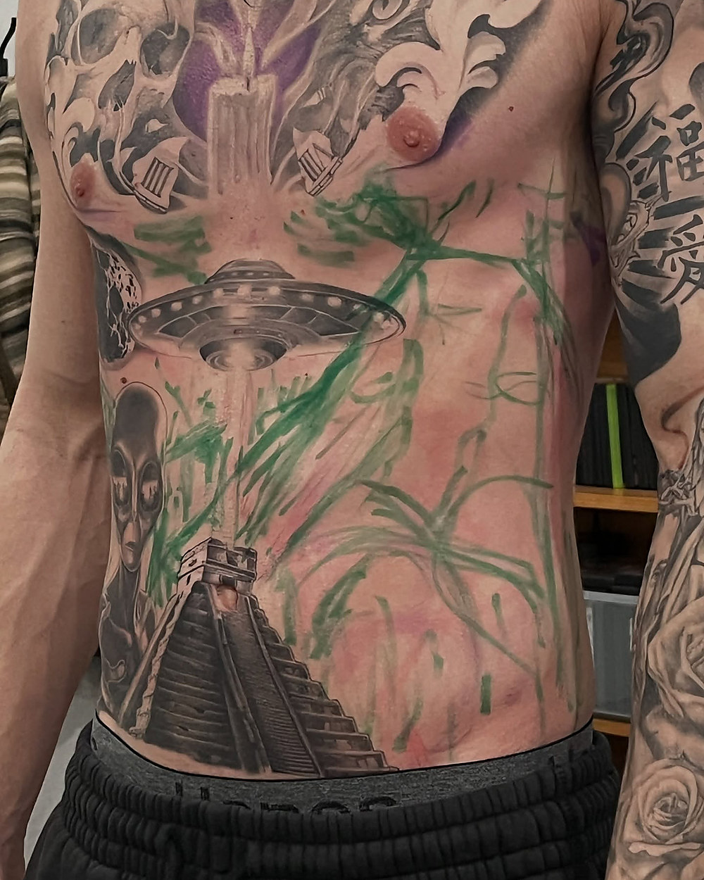 A stomach piece in progress, a pyramid under a UFO in black and grey, by Owen Lewis